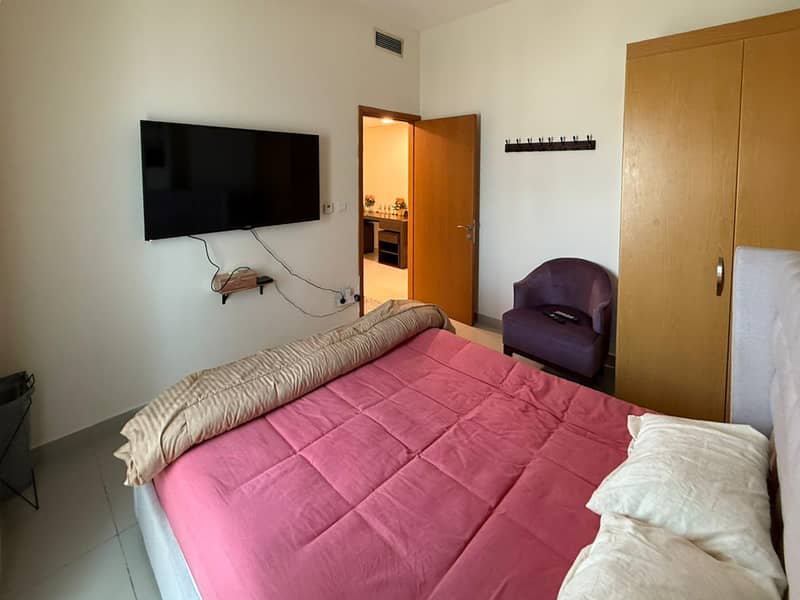 12 Bedroom with pink bedding, wall-mounted TV and purple armchair near an open door.