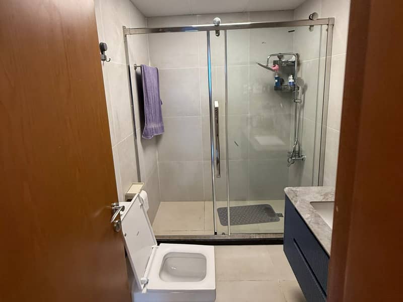 14 Bathroom with glass shower enclosure, toilet and vanity seen through a wooden doorway.